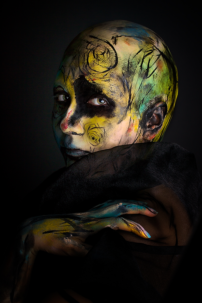 Abstract body art photography featuring model Celine M. adorned in swirling strokes of vibrant greens, yellows, blues, and reds, with a bold baldcap accentuating the canvas.