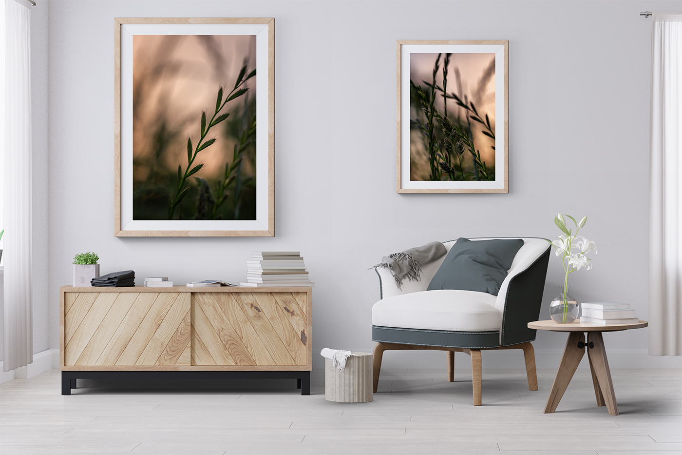 Two framed artworks, 'Nightly Breeze II' and 'Nightly Breeze I,' hang in light wooden frames on a white wall above a white and grey armchair. A wooden credenza with stacks of books and a small coffee table complete the scene.