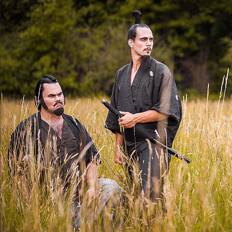 An image showing Minamoto no Yorimitsu and Watanabe no Tsuna, two Japanese samurai, standing in a wheat field. Both are adorned in traditional Japanese attire and hairstyles, created by makeup artist Anett Alexandra Bulano to reflect the characters from the Tsuchigumo Sōshi folktale.