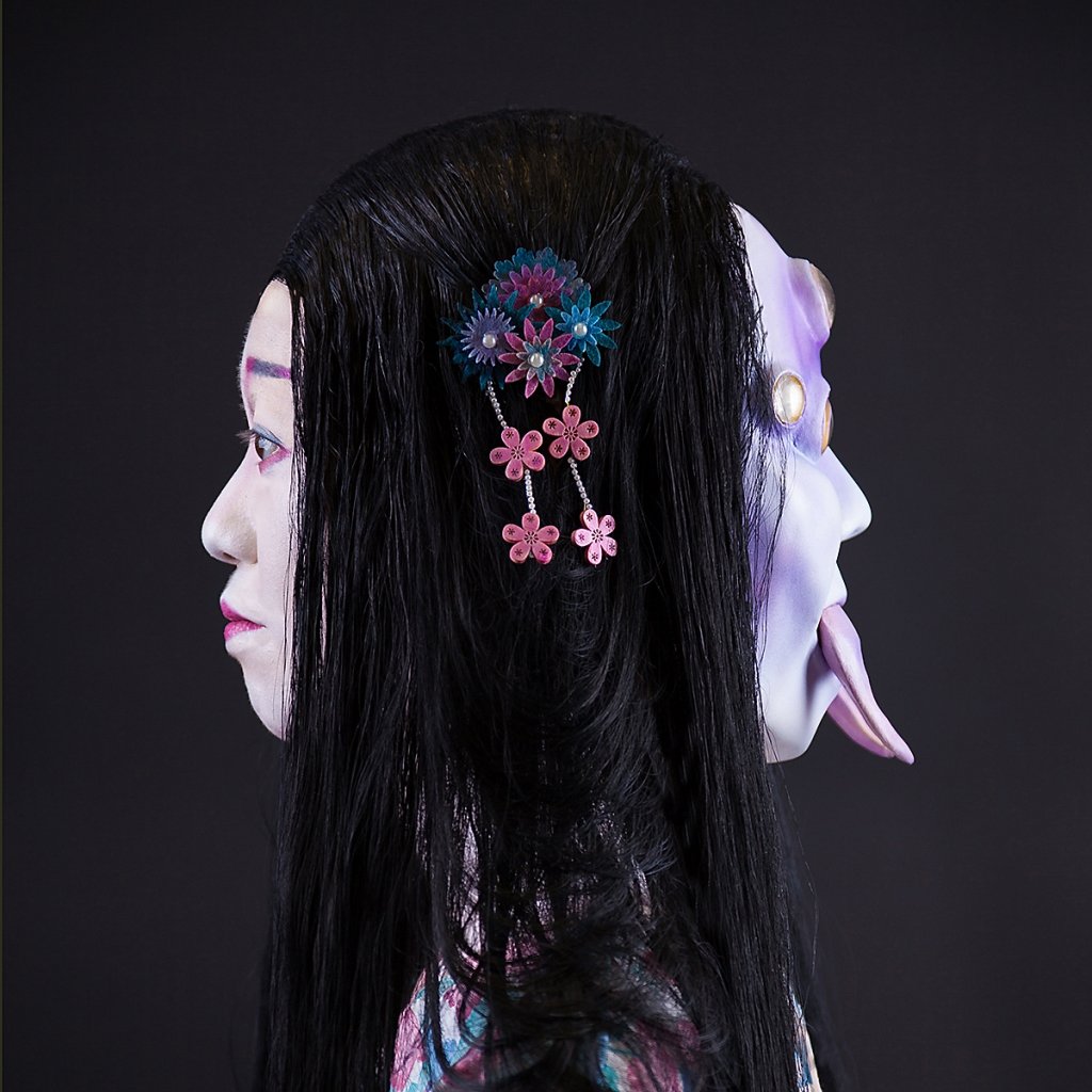 Side profile of a geisha adorned with traditional makeup and a Heian-period wig, juxtaposed with a spider mask featuring six yellow eyes and fangs. Created by makeup artist Anett Alexandra Bulano, inspired by Japanese folklore.