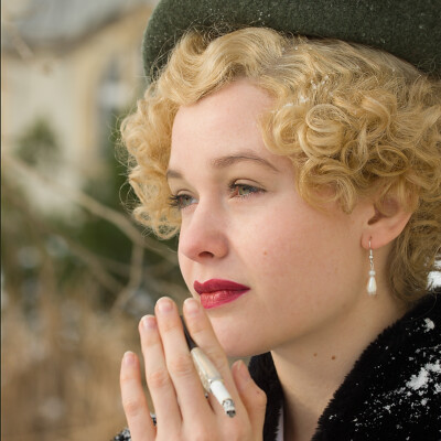 "Captivating elegance captured in the essence of the 1930s. 🎩✨ Lena D. channels timeless sophistication with a touch of modern flair, styled and photographed by Anett Alexandra Bulano. #VintageStyle #MarleneInspired" "Half-close portrait of Lena D. in vintage-inspired attire against a black background, wearing a green barrett hat and brown Marlene pants. Styled and photographed by Anett Alexandra Bulano."